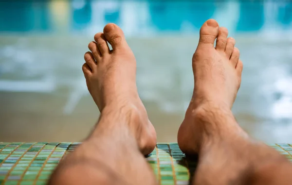 Hombre pies desnudos sentado en el banco en la piscina cubierta  . — Foto de Stock