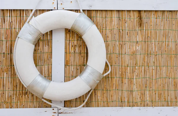 Einzelne weiße Rettungsboote, die an einer Schilfwand am Meeresufer hängen . — Stockfoto