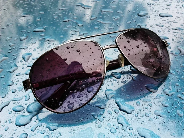 Mavi arkaplanda yağmur damlalarıyla kaplı güneş gözlüklerinin yakın çekimi