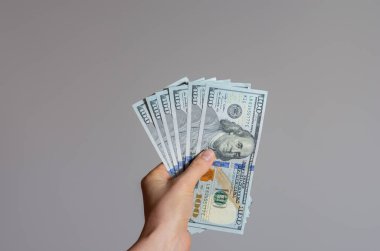 Gri bir arkaplanda 100 dolarlık banknotları tutan bir kadının el resmi. Coronavirüs 'ün Amerika Birleşik Devletleri' ndeki ekonomik etkisi .