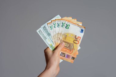 Gri arka planda bir avuç avro banknotunu tutan bir kadının el görüntüsü. Coronavirüs 'ün Avrupa Birliği üzerindeki ekonomik etkisi .