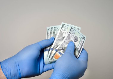 Eline ameliyat eldiveni takmış bir adam para banknotlarını sayıyor. Kovid 19 ve bakteri bulaşmasına karşı koruma.