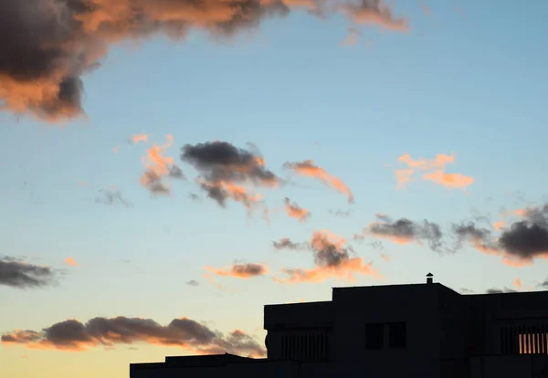 Gün batımında turuncu ve siyah bulutlarla çevrili bir binanın silueti. .