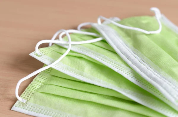 Ahşap arka planda yeşil renkli tek kullanımlık yüz maskesi. Grip ve virüsün yayılmasını önlemek için sağlıklı alışkanlıklar .