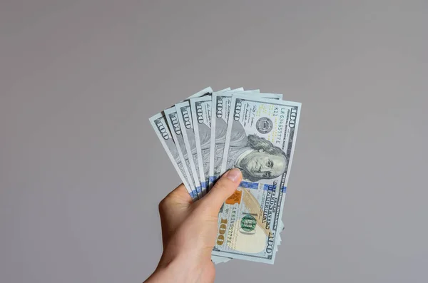 Gri bir arkaplanda 100 dolarlık banknotları tutan bir kadının el resmi. Coronavirüs 'ün Amerika Birleşik Devletleri' ndeki ekonomik etkisi .