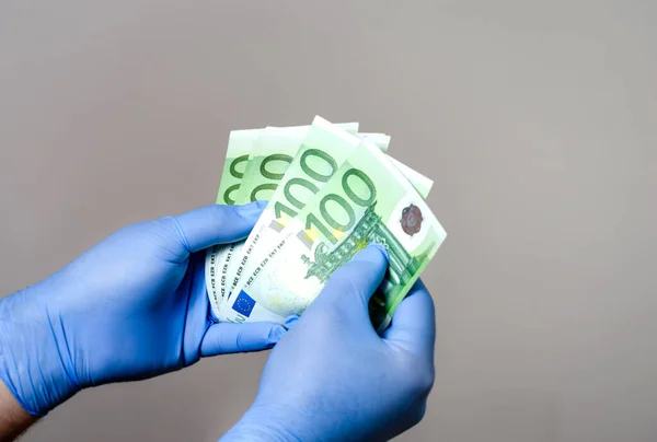 Elinde ameliyat eldiveni olan bir adam euro banknotlarını sayıyor. Coronavirus sırasında covid-19 ve bakteri ekonomisine karşı korunma. . 