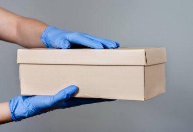 Ellerinde ameliyat eldivenleri olan bir kadın ya da erkek hediye paketi tutuyor. Covid-19 salgını sırasında çevrimiçi alışveriş dağılımı için koruyucu tedbirler .