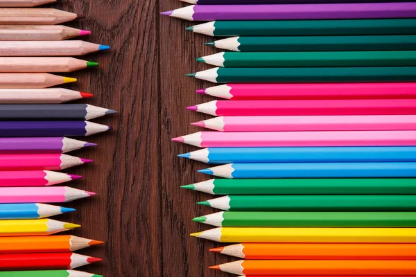 Colored pencils on brown background lying in opposite sides of wooden table — Stock Photo, Image