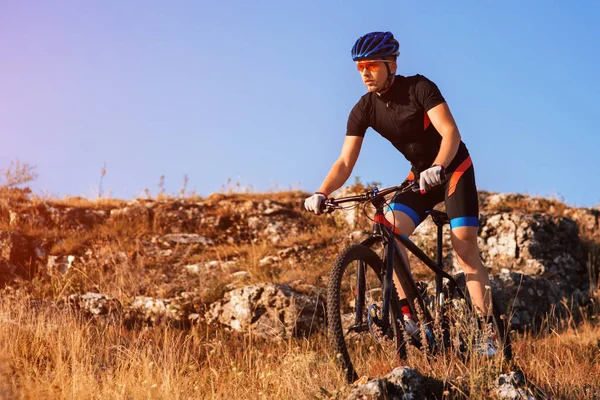 Ciclista profissional montando a bicicleta no Rocky Trail. Esportista no capacete e óculos de sol . — Fotografia de Stock