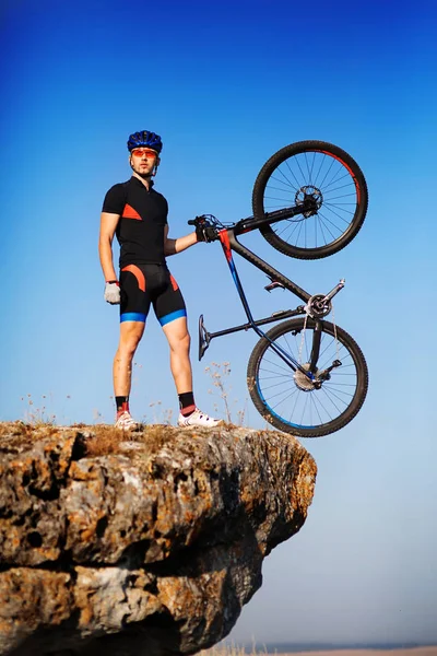 Ποδηλάτης άνθρωπος κρατά ποδήλατο στην κορυφή ενός λόφου ενάντια όμορφο μπλε ουρανό. — Φωτογραφία Αρχείου