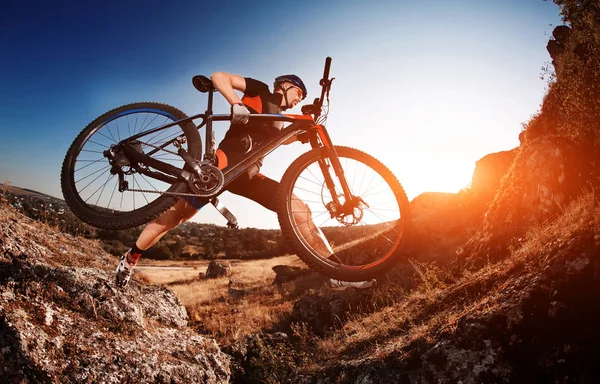 Professional wielrenner neemt zijn fiets omhoog de Rocky Trail bij avond. Extreme Sport Concept. Lage hoek en fisheye. — Stockfoto