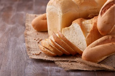 Ahşap masa üzerinde çuval bezi üzerinde beyaz ekmek ürün yelpazesine sahip. Dilim ekmek ve baget.