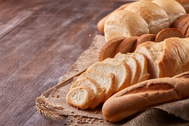 Ahşap masa üzerinde çuval bezi üzerinde beyaz ekmek ürün yelpazesine sahip. Dilim ekmek ve baget.