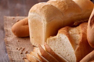 Ahşap masa üzerinde çuval bezi üzerinde beyaz ekmek ürün yelpazesine sahip. Dilim ekmek ve baget.