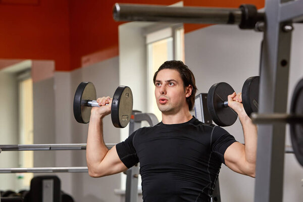 Personal Trainer in black t-shirt doing sitting dumbbell curls for training his biceps, in a gym