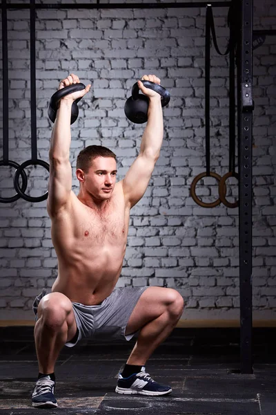 Addestramento Crossfit. Fitness uomo in pantaloncini grigi che fa un allenamento con i pesi sollevando kettlebells . — Foto Stock