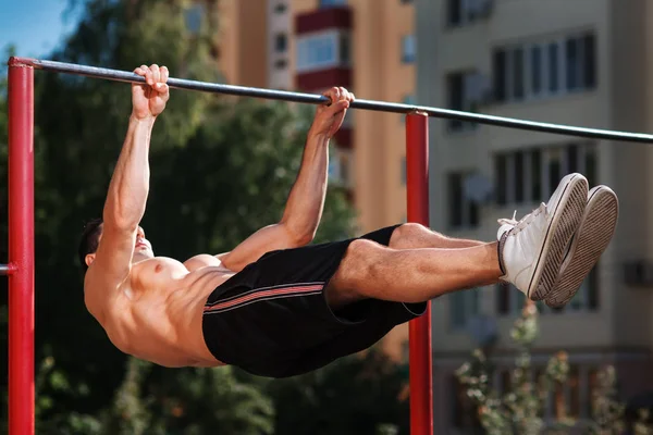 Giovane uomo muscoloso costruire facendo pull up esercizi sulla barra orizzontale all'aperto . — Foto Stock