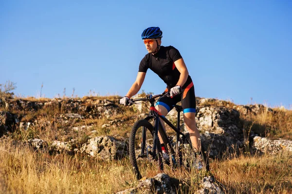 Ciclista profesional montando la bicicleta en el sendero rocoso. Deportista en el casco y gafas de sol . — Foto de Stock