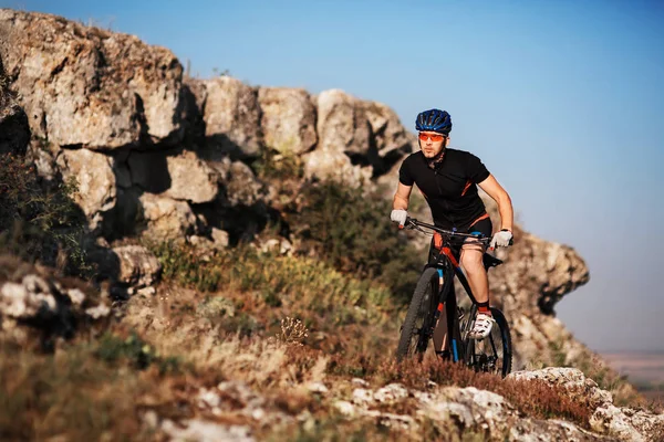 Ciclista en ropa deportiva negra Montar en bicicleta en el sendero rocoso. Concepto de deporte extremo. Espacio para el texto . — Foto de Stock