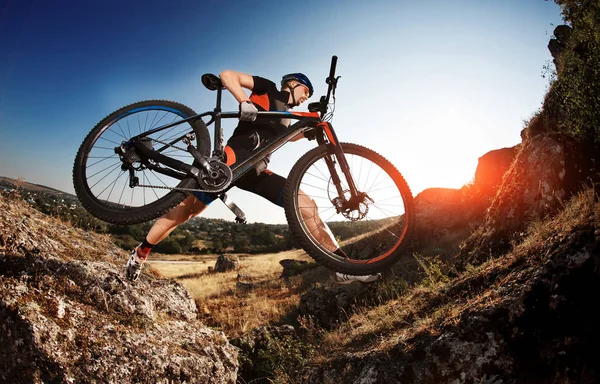 Professional wielrenner neemt zijn fiets omhoog de Rocky Trail bij avond. Extreme Sport Concept. Lage hoek en fisheye. — Stockfoto