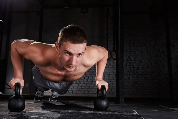 Sportsman fare push-up esercizio con kettlebell in un allenamento crossfit contro muro di mattoni — Foto Stock