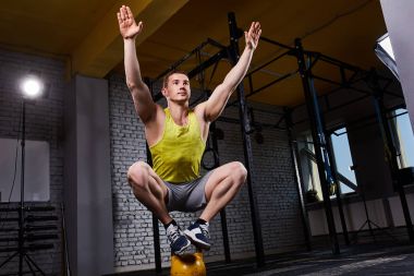 Kettlebell üzerinde iki ayak üzerinde çömelme sırasında uygun spor egzersizleri yaparken genç atletik erkek.