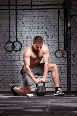 Kettlebell kolları haç üzerinde tutan genç sporcu spor salonu kat tuğla duvarın uygun.