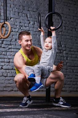 Mutlu baba ve gimnastic halkalar ile egzersiz ve tuğla karşı gülümseyen küçük oğul salonda duvar.