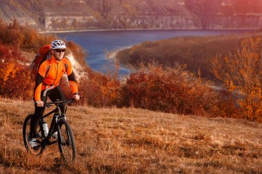 Turuncu jacketr karşı güzel manzara nehir altında tepe üzerinde Bisiklete binmek bisikletçi.