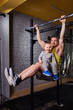 Çekme işi genç mutlu baba Çubuğu'nda ups bacaklarını çapraz, oğlu ile uygun tuğla duvara spor salonu.