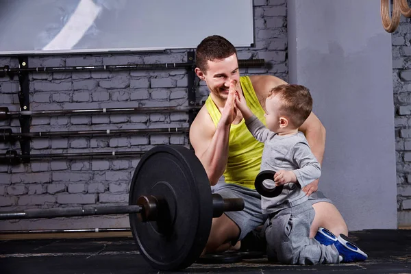 Mutlu baba ve oğlu haç barbell ile portre spor salonu tuğla duvara uygun.