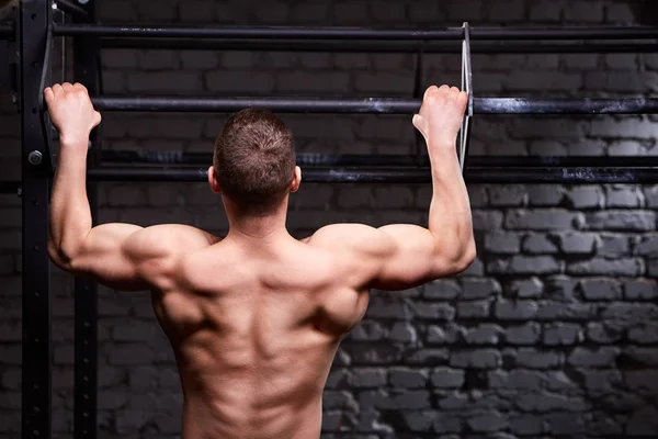 リア クロス フィット ジムでレンガの壁に対して水平バーで演習を行って筋肉の男性の写真を見る. — ストック写真
