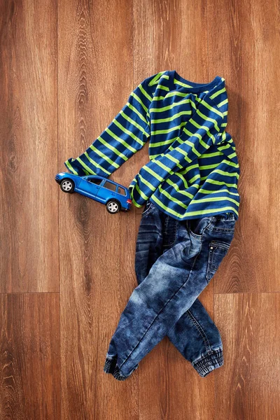 Chaqueta infantil y jeans con coche azul de juguete sobre fondo de madera . — Foto de Stock
