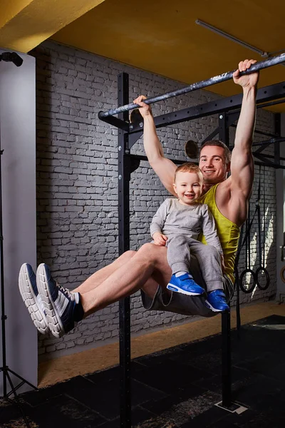 Çekme işi genç mutlu baba Çubuğu'nda ups bacaklarını çapraz, oğlu ile uygun tuğla duvara spor salonu.