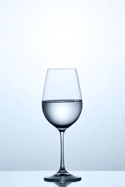 Чистая вода в стационарном бокале, стоя на чистом стекле на светлом фоне . — стоковое фото