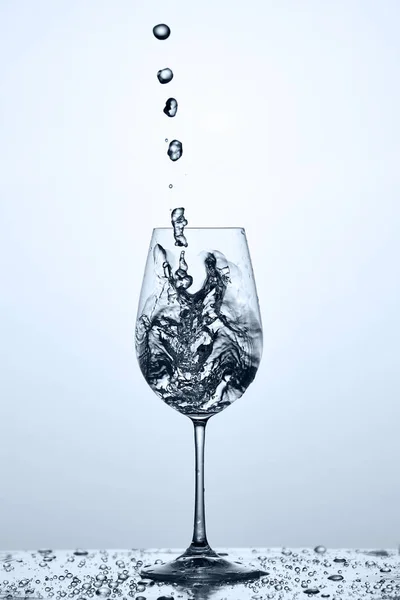 Pouring and splashing cleaner drinking water on a wineglass while standing against light background.