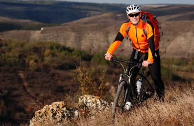 Güzel manzara karşı bir tepenin üst kısmında kırmızı sırt çantası ayakta ile sportif bisikletçi.
