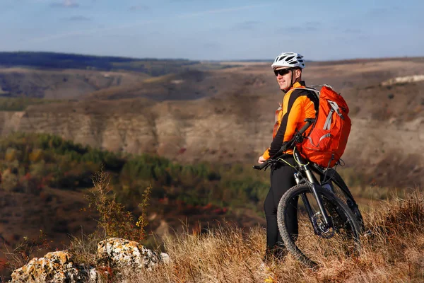 Jovem ciclista fica com a bicicleta de montanha na trilha rochosa de verão contra a bela paisagem com montanha . — Fotografia de Stock