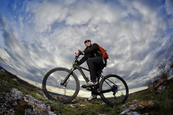 Portret młodego kolarza stojąc z roweru na skałach przeciwko dramatyczne niebo z chmurami. — Zdjęcie stockowe