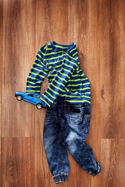 Ropa para niños y coche de juguete azul sobre fondo de madera . — Foto de Stock