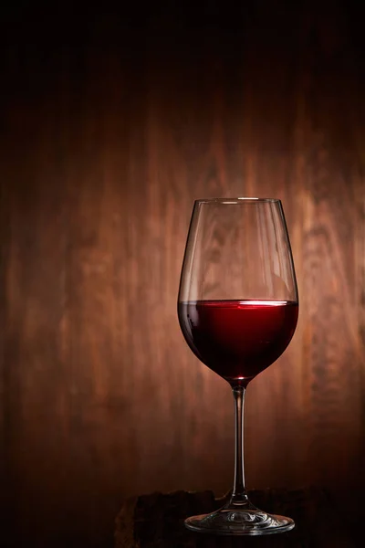 Verre à vin rouge à moitié plein et fragile, debout sur un fond en bois . — Photo