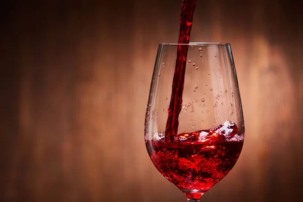 Gros plan sur le vin rouge savoureux versé dans le verre à vin pur fragile debout sur un fond en bois . — Photo