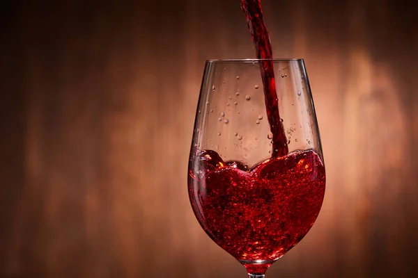 Gros plan sur le vin rouge savoureux versé dans le verre à vin pur fragile debout sur un fond en bois . — Photo