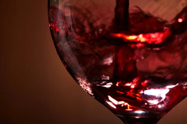 Gros plan de vin rouge vif versé dans le verre à vin et éclaboussures abstraites sur fond brun . — Photo