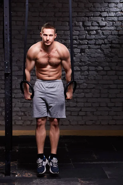 Junger Fitness gutaussehender Mann macht Tauchübung mit Ringen gegen Ziegelwand in der Crossfit-Turnhalle. — Stockfoto