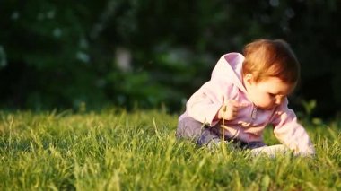 Mutlu küçük bebek kız parkta yeşil çimenlerin üzerinde günbatımında oturmuş.