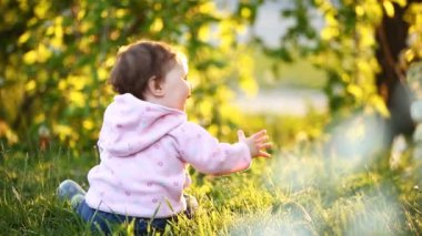 Şirin kız bebek yeşil çimenlerin üzerinde park ar günbatımında oturan arkadan görünüş.