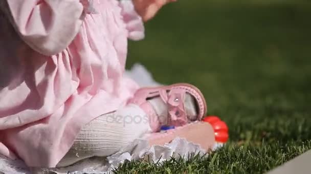 Close-up of the beautiful baby-girl seating on the green grass in the park. — Stock Video