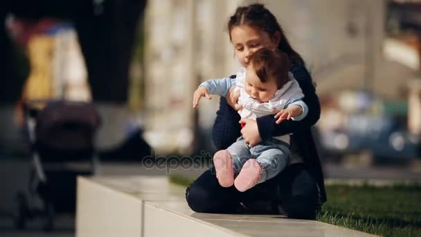 Lilla söta tjejen kramar hennes syster baby-flicka i parken vid solsken dag. — Stockvideo