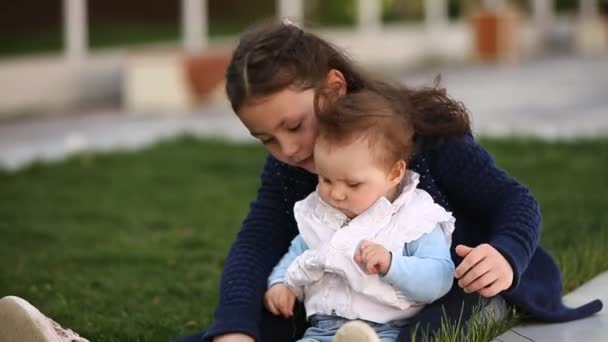 Pequeña niña bonita sentada sobre hierba verde en el parque al atardecer . — Vídeo de stock